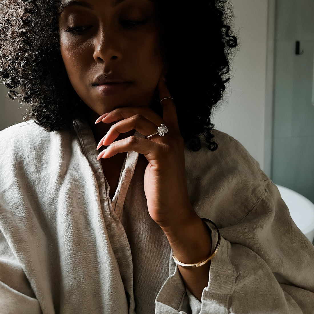 Curly haired woman wearing the Piglet in Bed oatmeal linen flax robe in bathroom.
