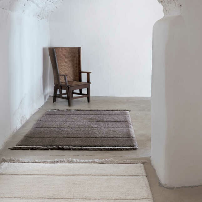 A minimalist space featuring two rugs from the Lorena Canals Steepe Collection, shown in sheep white and sheep brown.