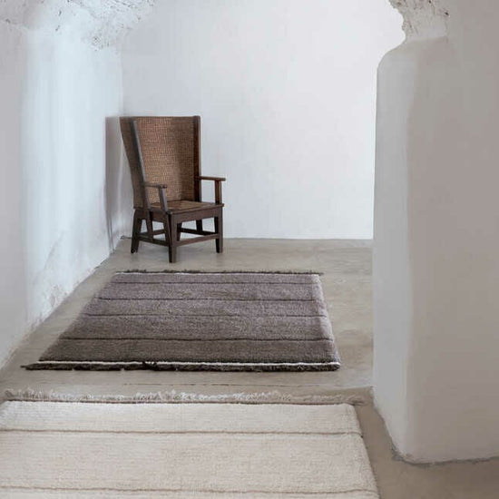 A minimalist space featuring two rugs from the Lorena Canals Steepe Collection, shown in sheep white and sheep brown.