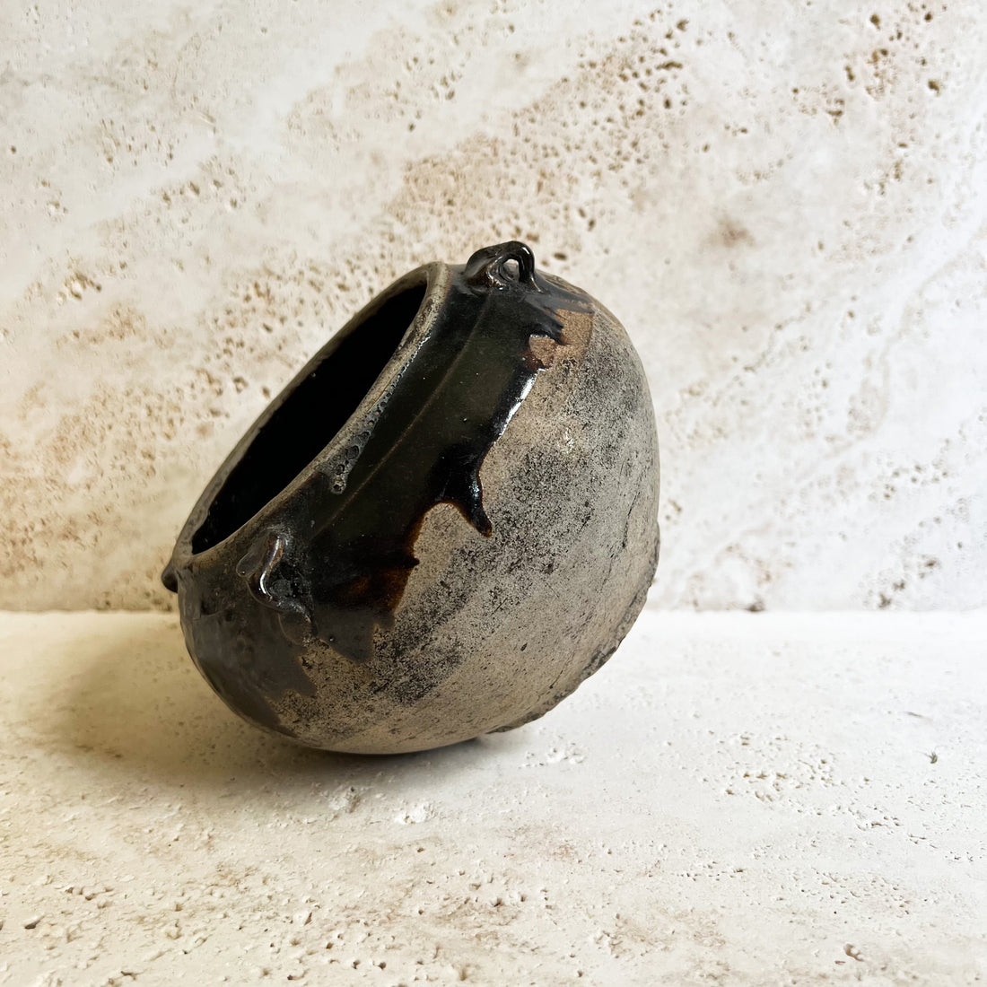 Antique brown Chinese pot filled with dried white German statice florals. The pot sits on a travertine stone.
