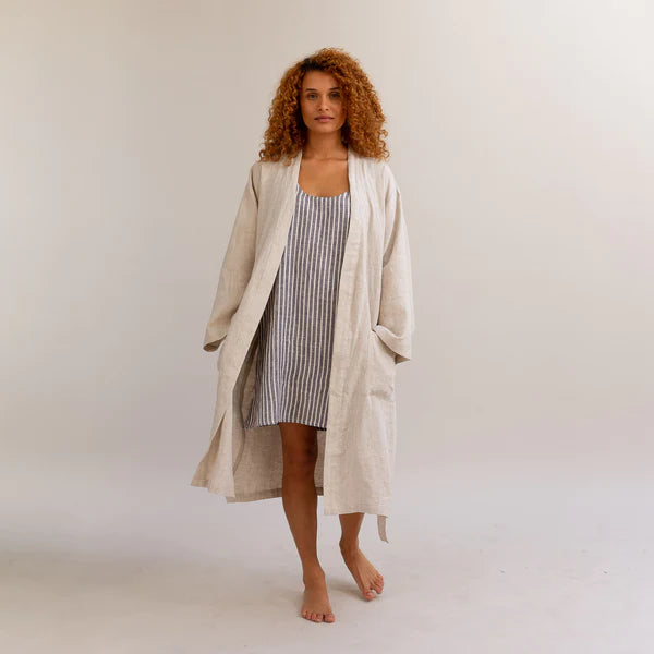 Curly haired woman wearing the Piglet in Bed oatmeal linen flax robe over a nightgown. 