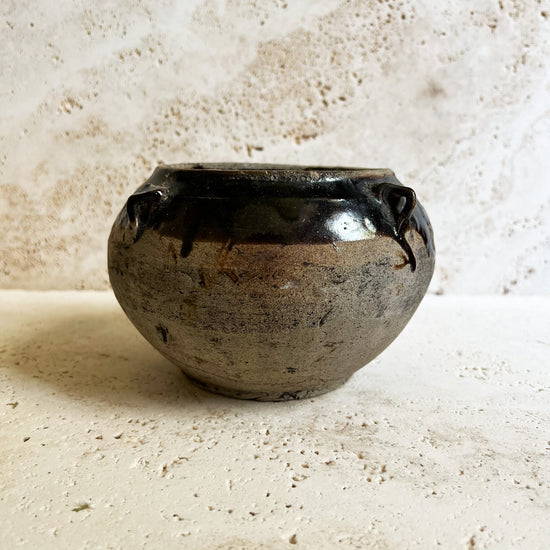 Antique brown Chinese pot that sits on a travertine stone.