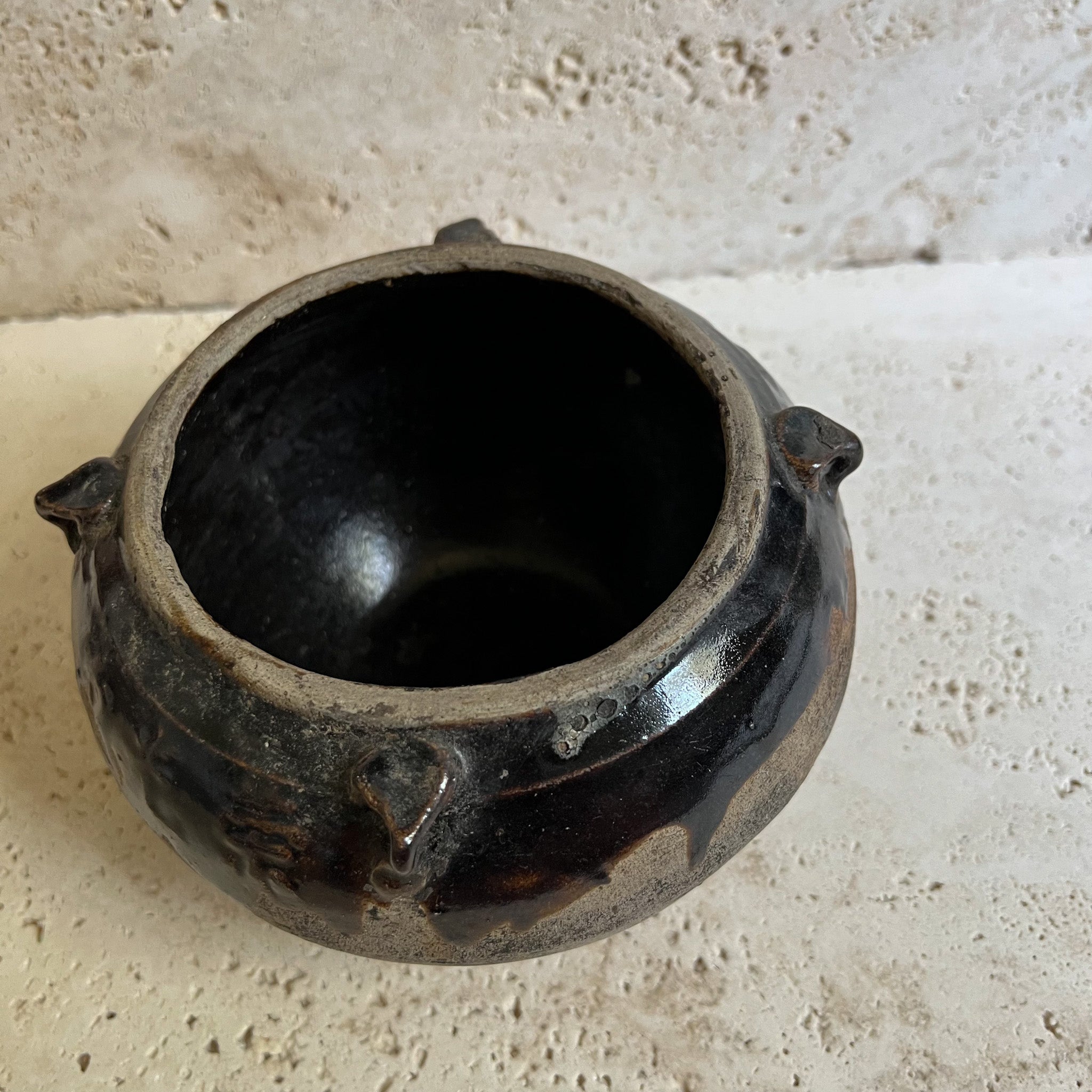Antique brown Chinese pot that sits on a travertine stone.
