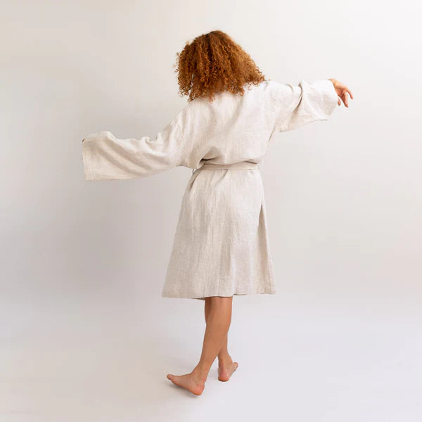 Curly haired woman showing the back view of a tied Piglet in Bed oatmeal linen flax robe.